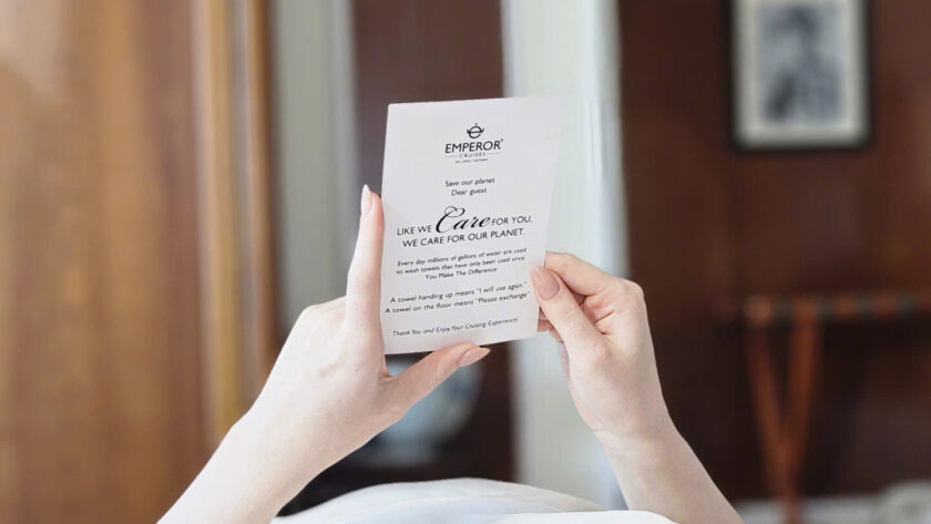 Guest reading a towel reuse card aboard Emperor Cruises Legacy, promoting responsible cruising in Bai Tu Long Bay.