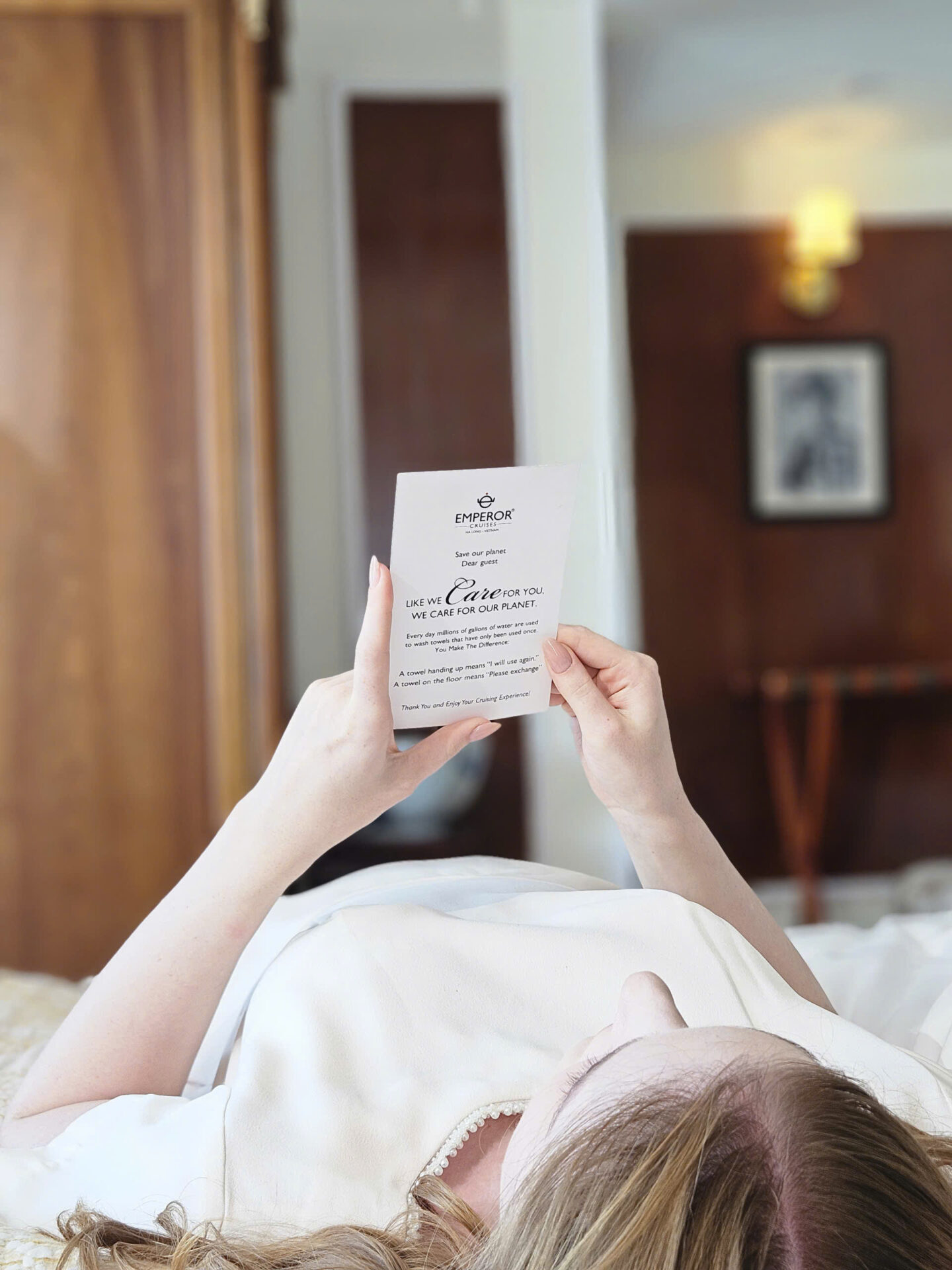 Guest reading a towel reuse card aboard Emperor Cruises Legacy, promoting responsible cruising in Bai Tu Long Bay.